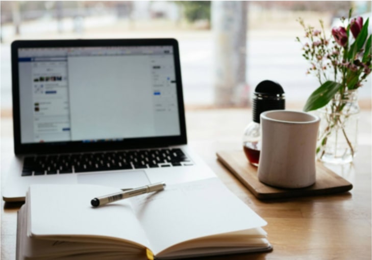 notebook sitting in front of open laptop with a coffee mug to the right